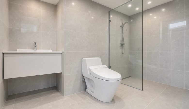 Salle de bains contemporaine lumineuse avec un WC japonais connecté blanc suspendu, une commande latérale discrète et un carrelage gris clair.
